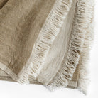 a reversible light brown and natural linen cotton throw blanket with a delicate fringe edge : close up view