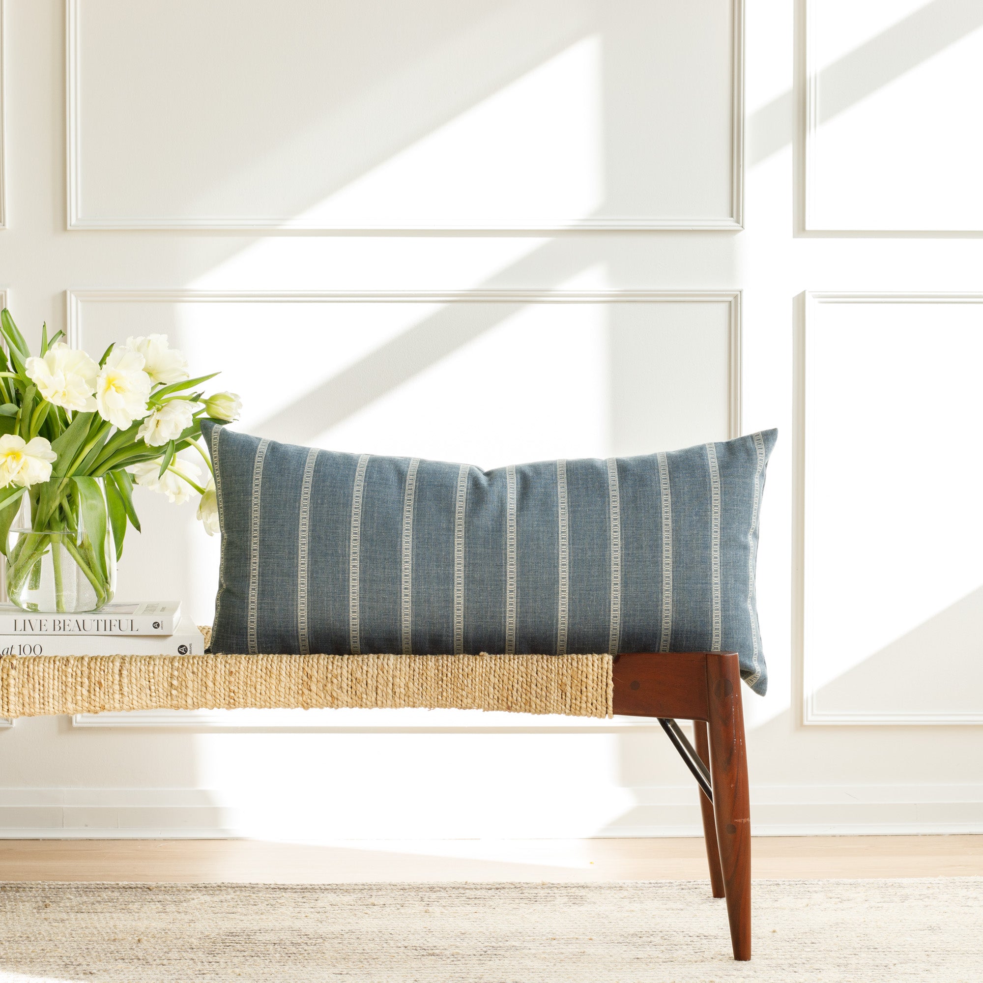 A blue and white striped large lumbar pillow, styled on a bench.