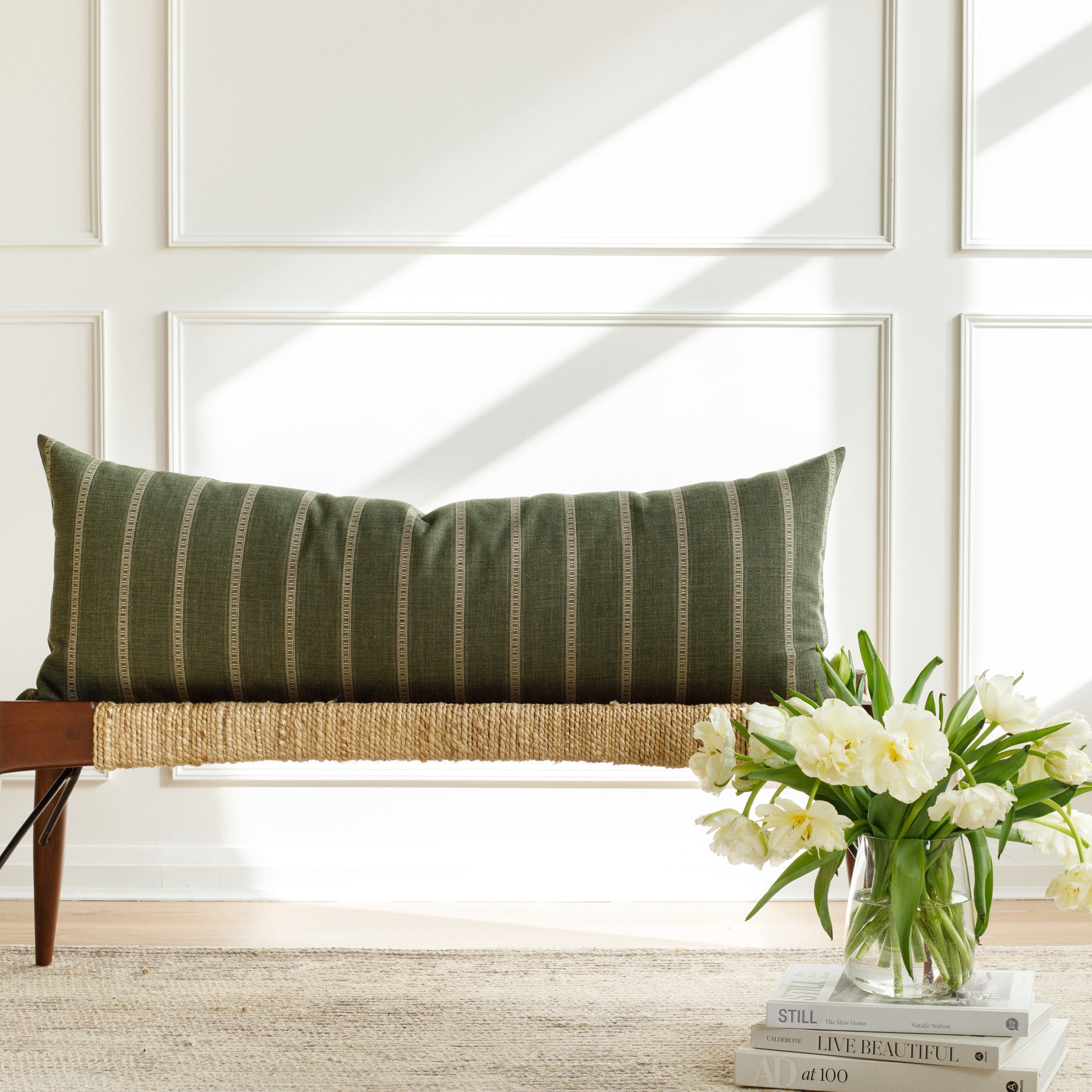 A green and beige striped bolster pillow from Tonic Living, styled on a bench.