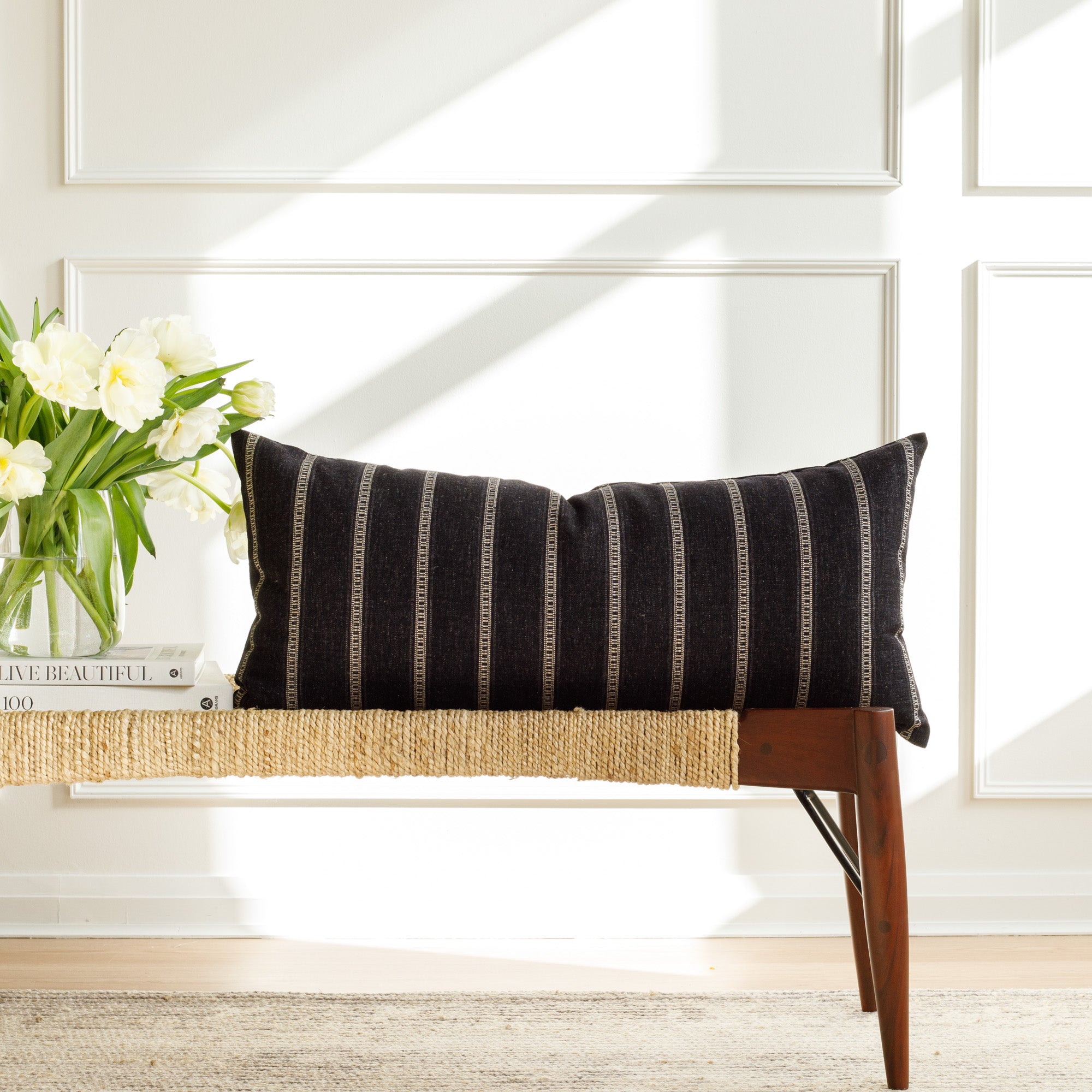 A black and white striped lumbar pillow from Tonic Living, styled on a bench.