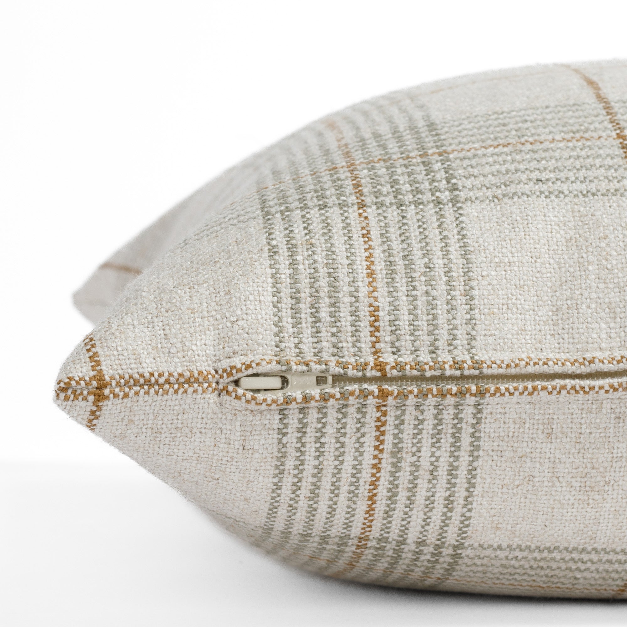 A beige, light green and tan plaid pillow: a close up zipper view.