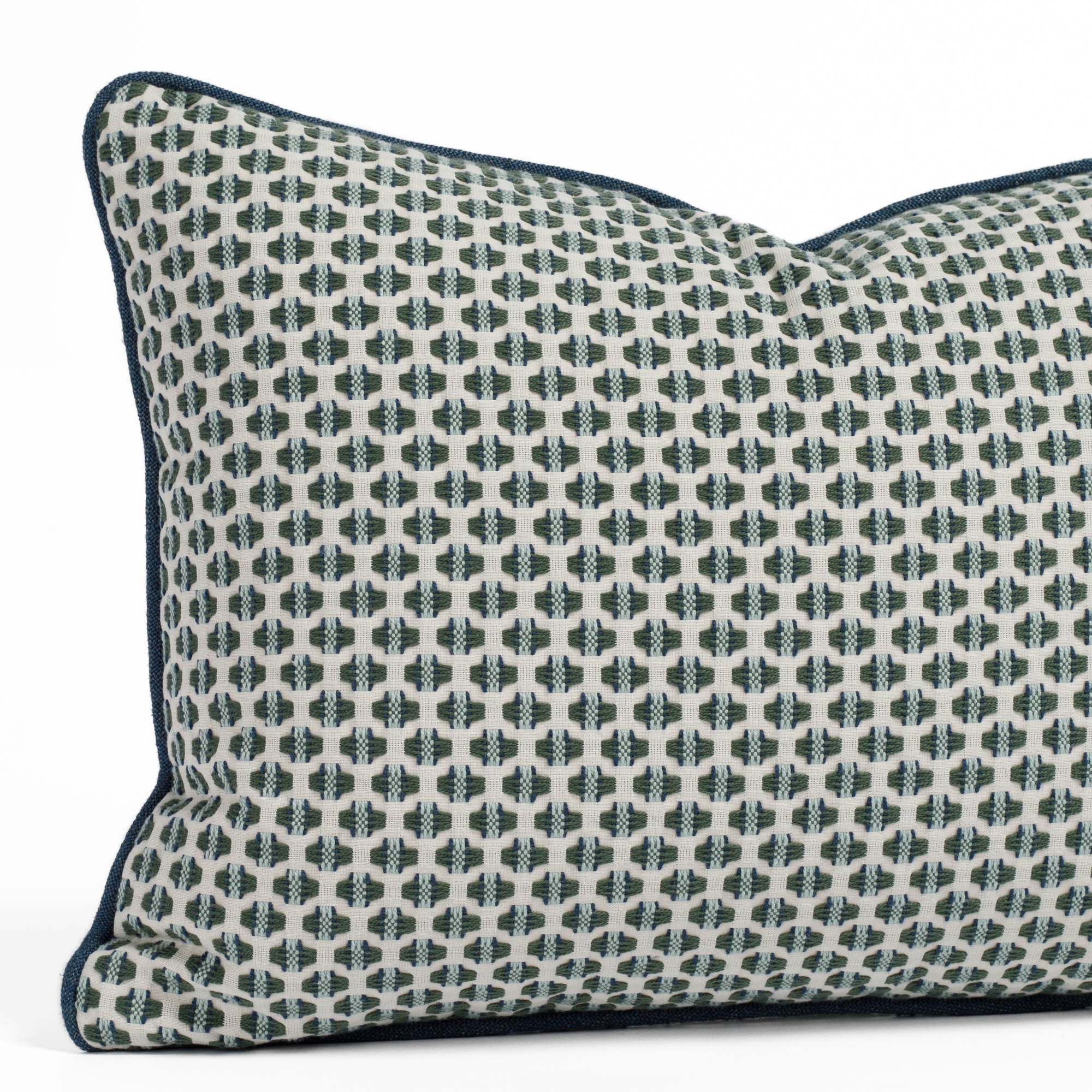 A white, sage green, sky blue and indigo geometric patterned pillow with blue piped edge: close up view.