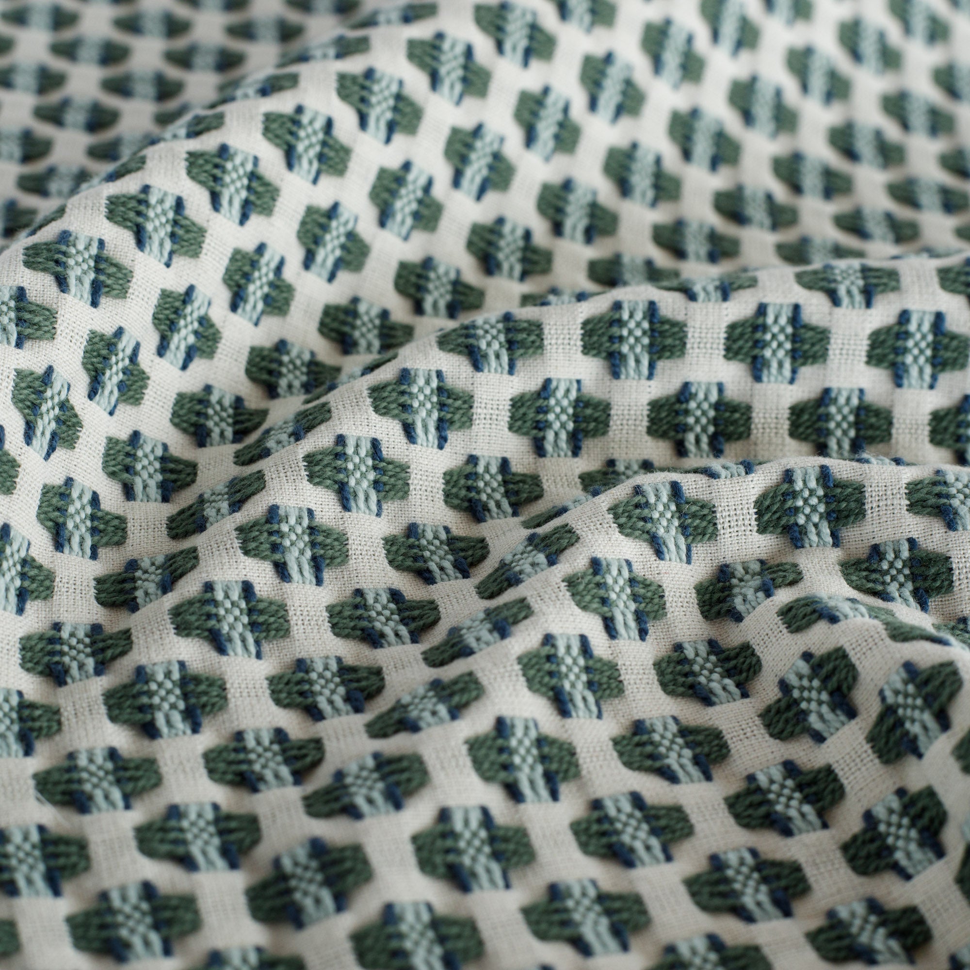 a cream, blue and green intricate woven small geometric patterned upholstery fabric : close up view