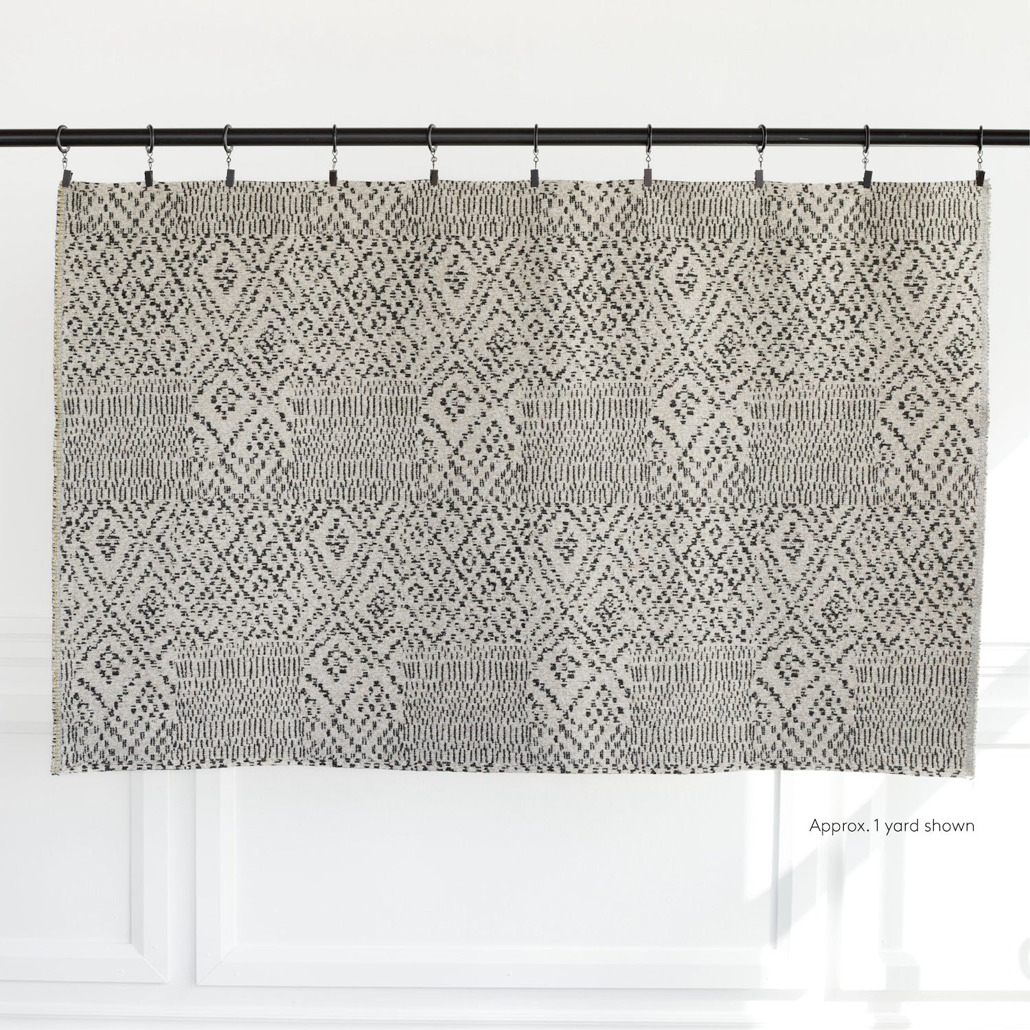 A yard of Tonic Living fabric in a beige and black pattern, hanging from curtain clips.