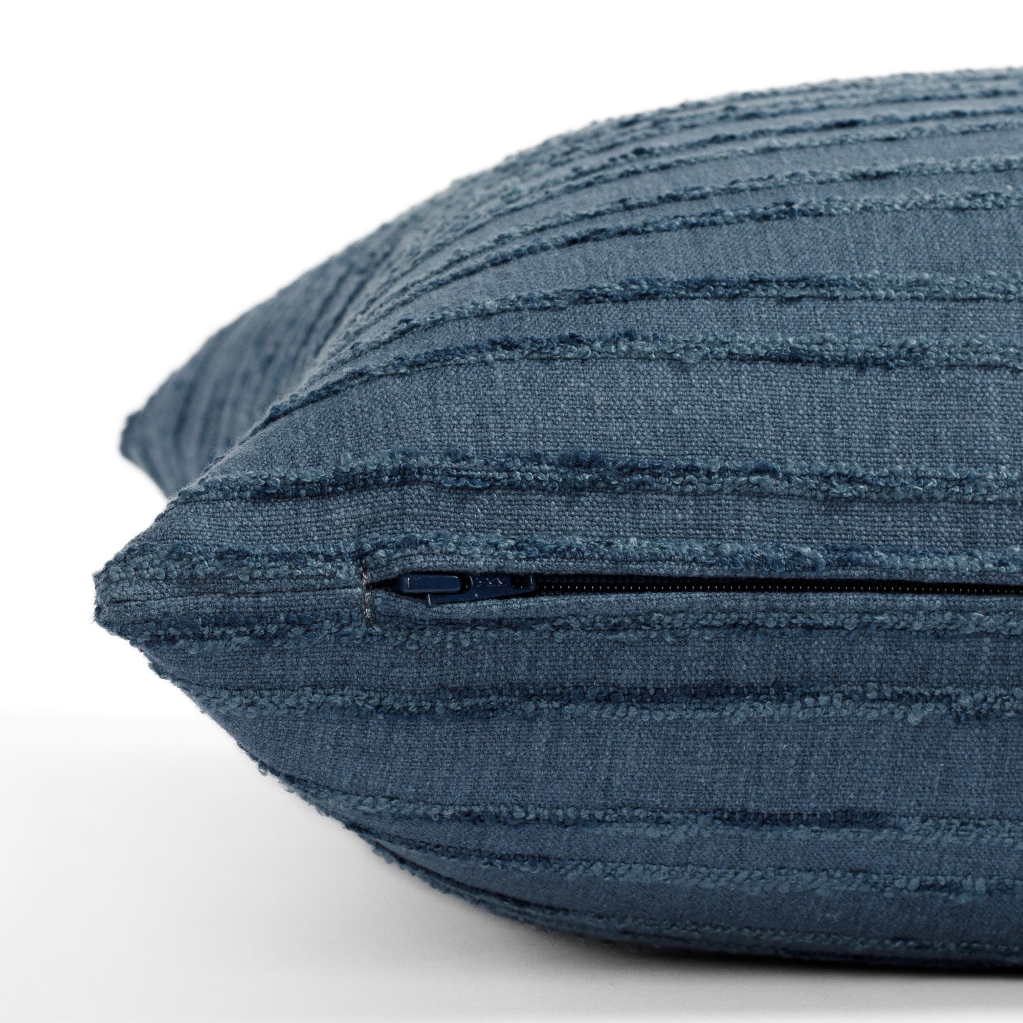 A medium blue pillow with bouclé stripes: close up zipper view.